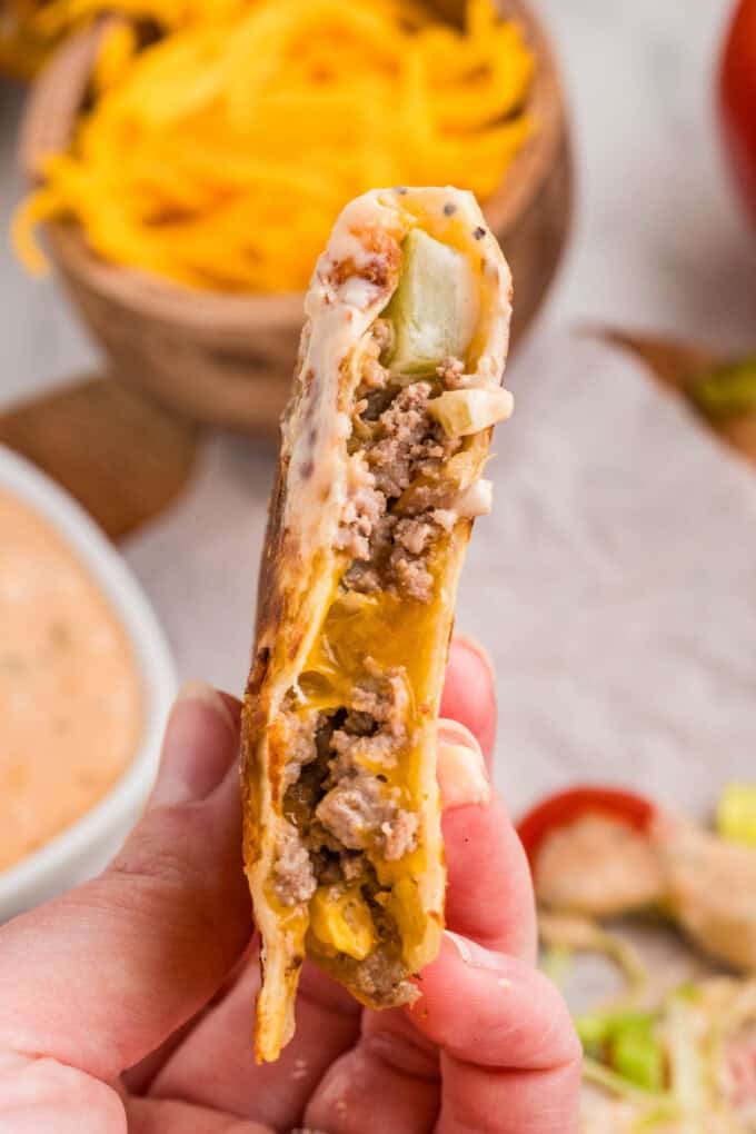 A side view of the filling of a cheeseburger quesadilla being held in a hand.