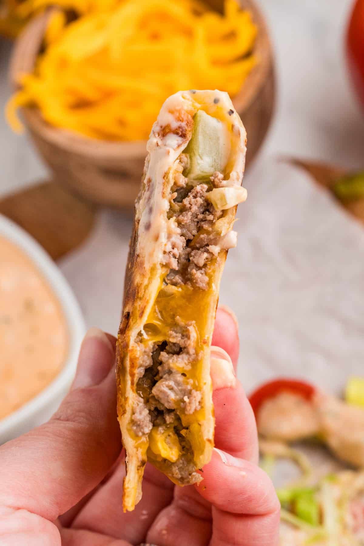 A side view of the filling of a cheeseburger quesadilla being held in a hand.