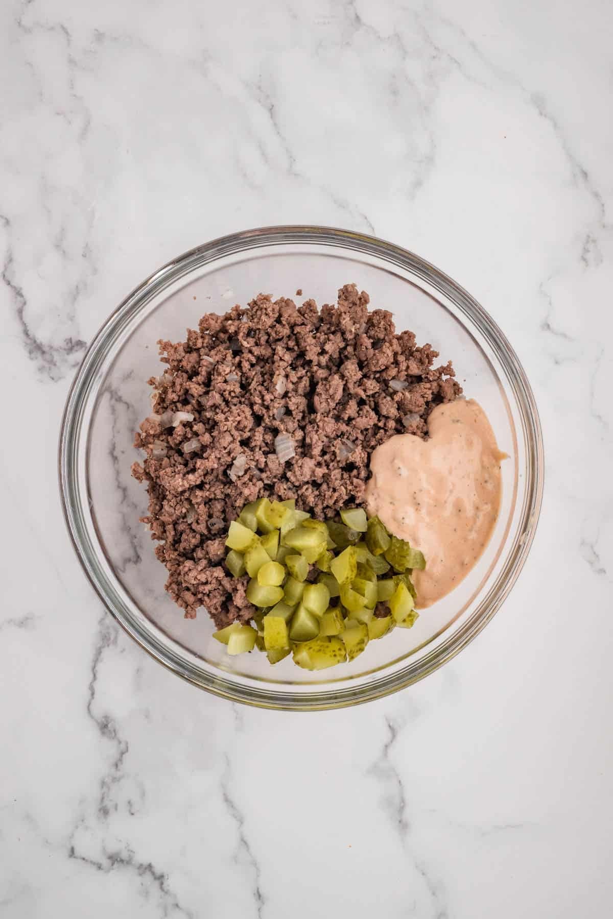 Adding chopped pickles to cooked ground beef with burger sauce.