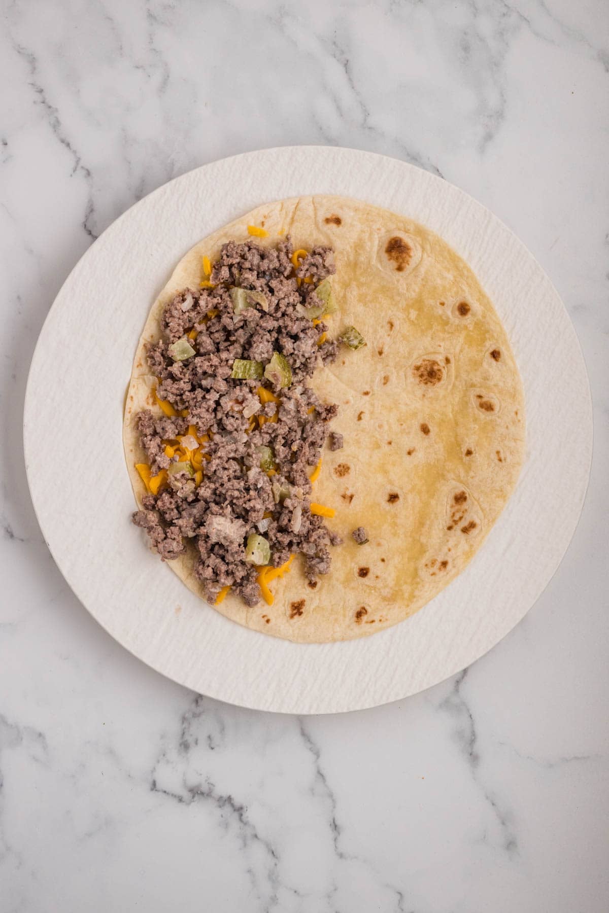 Layering shredded cheese and seasoned meat on a flour tortilla on a plate.