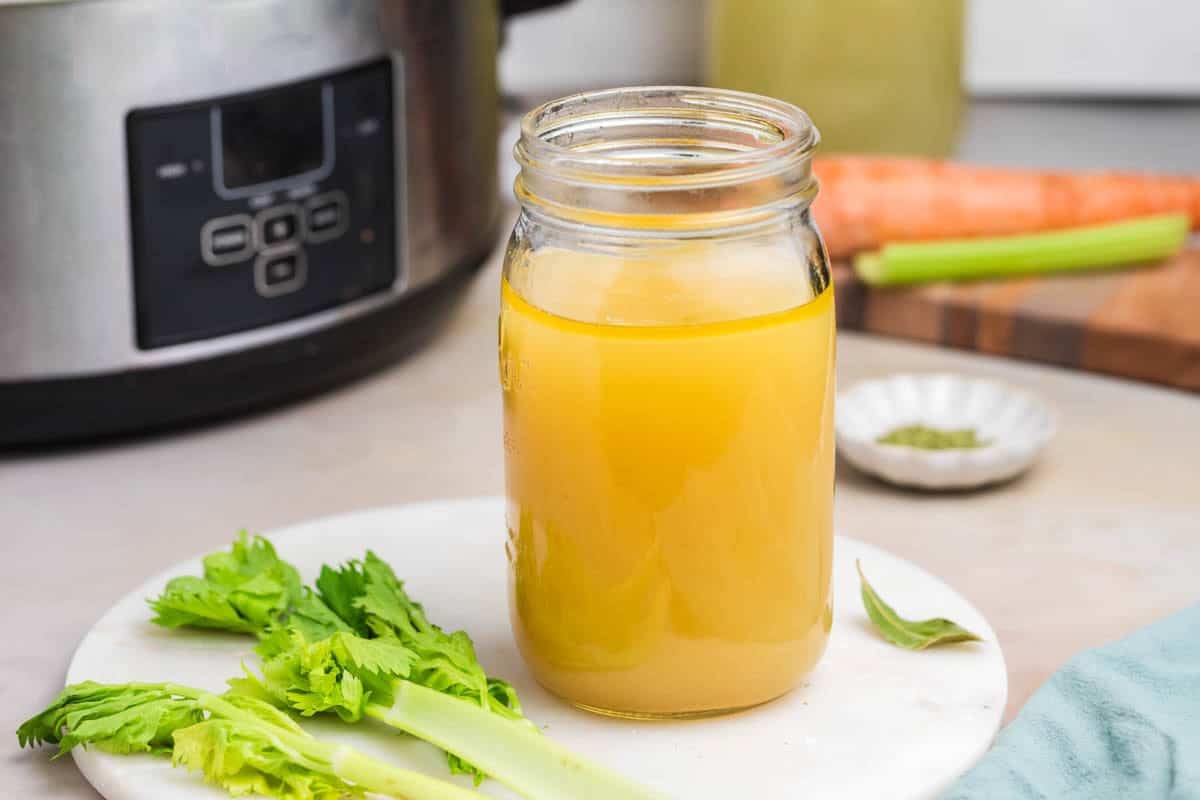 A jar of homemade chicken broth in front of a slow cooker.