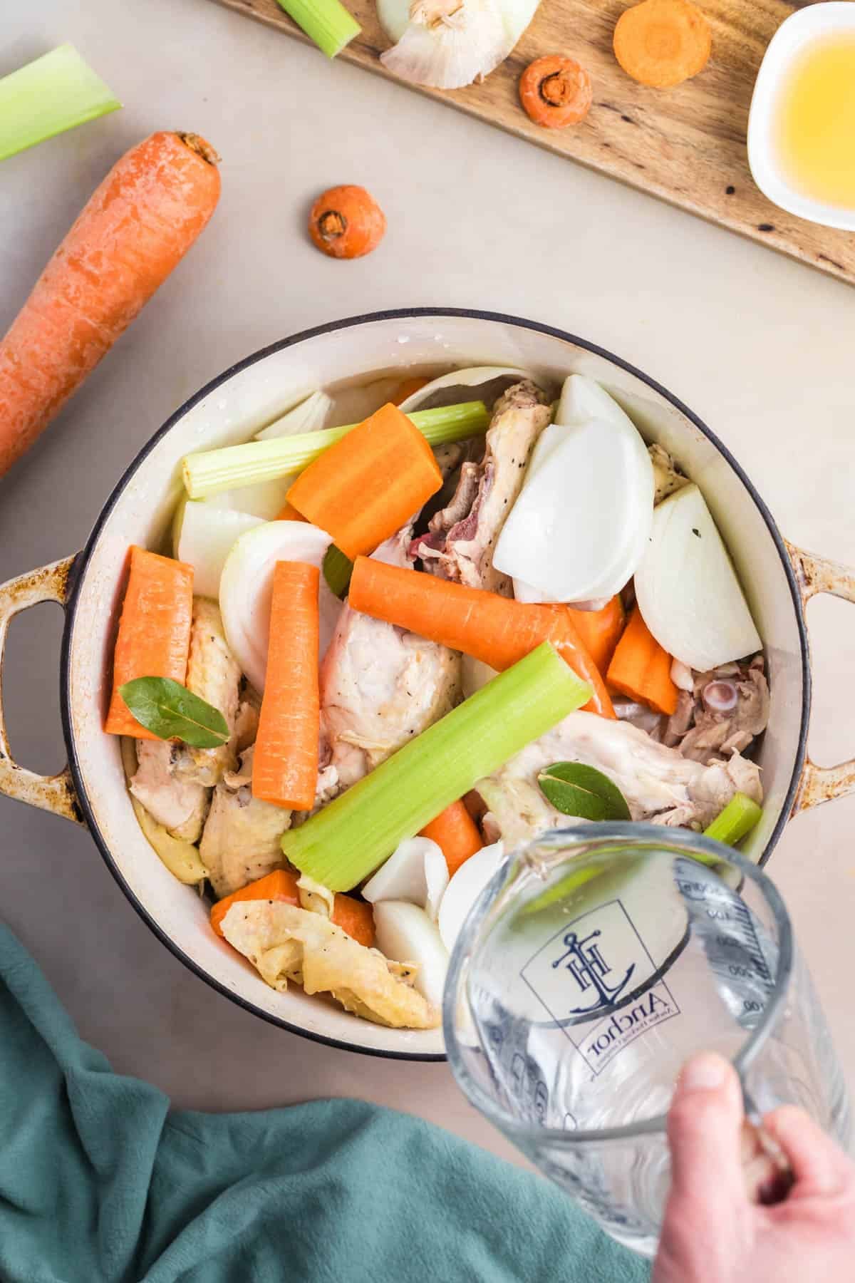 Water being poured into a pot of ingredients for making homemade chicken broth.