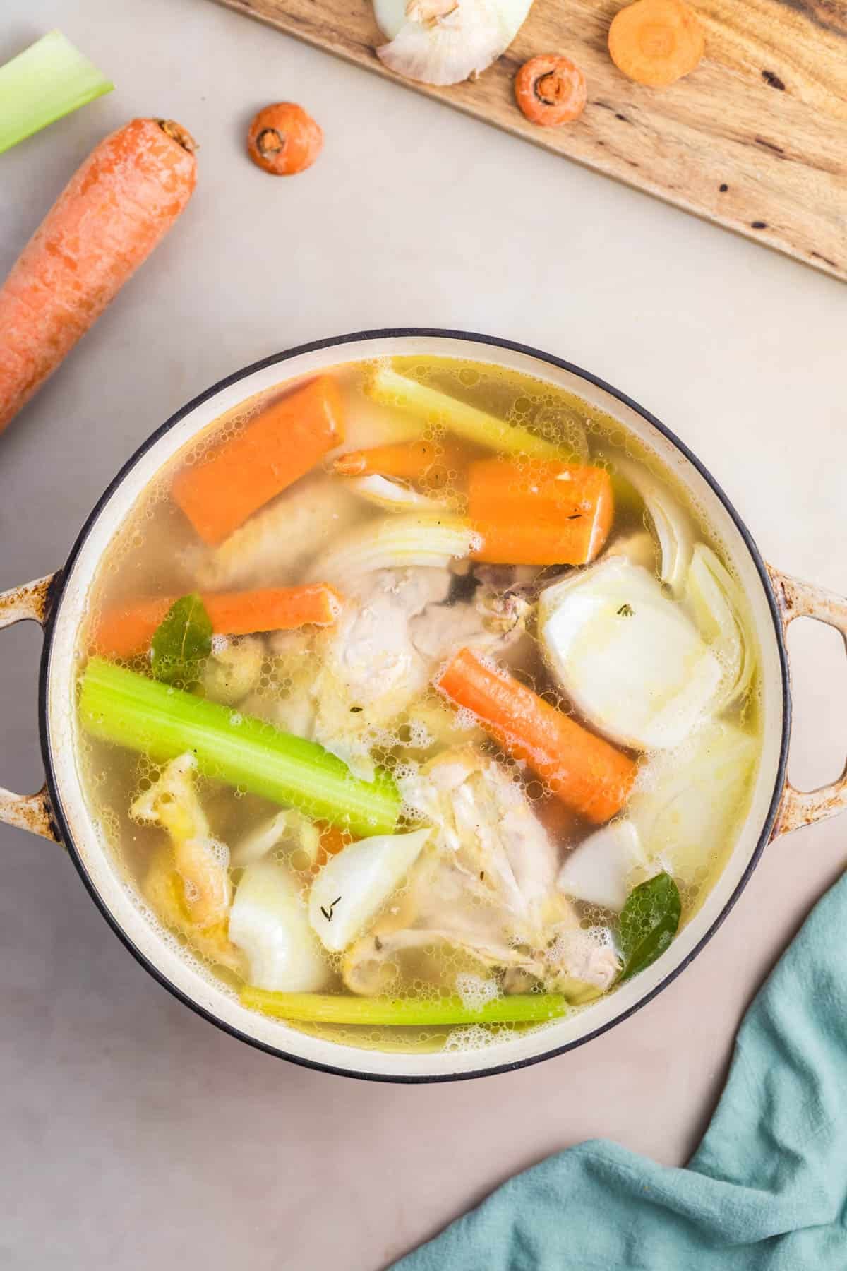 Combining carrots, celery, onions, and chicken bones in a pot to make homemade chicken broth.