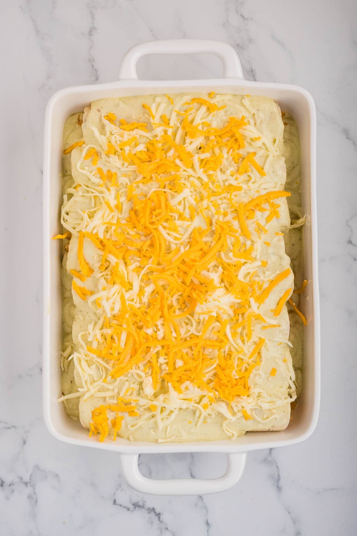 Adding shredded cheese on top of chicken enchiladas before baking.