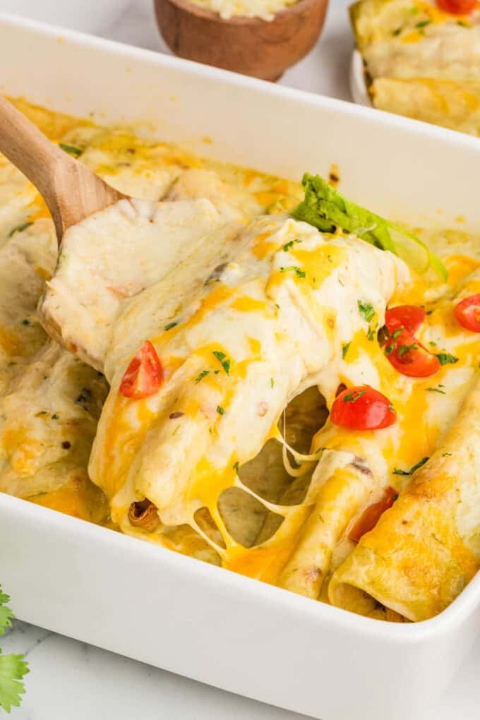 A spatula lifting an enchilada from a baking dish.