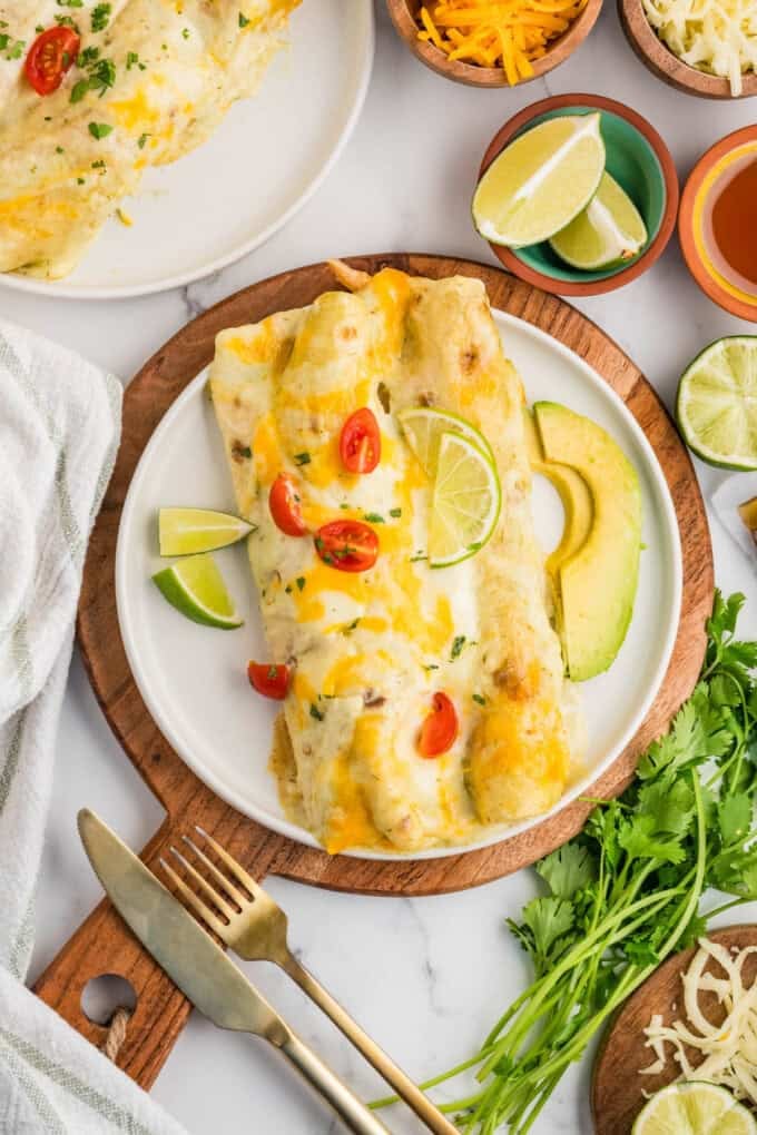 An overhead image of two honey lime chicken enchiladas on a plate surrounded by toppings.