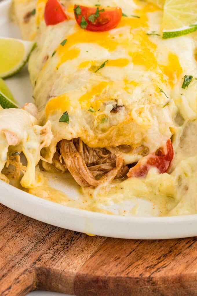 A honey lime chicken enchilada on a plate with a few bites taken out of it so you can see the filling inside.
