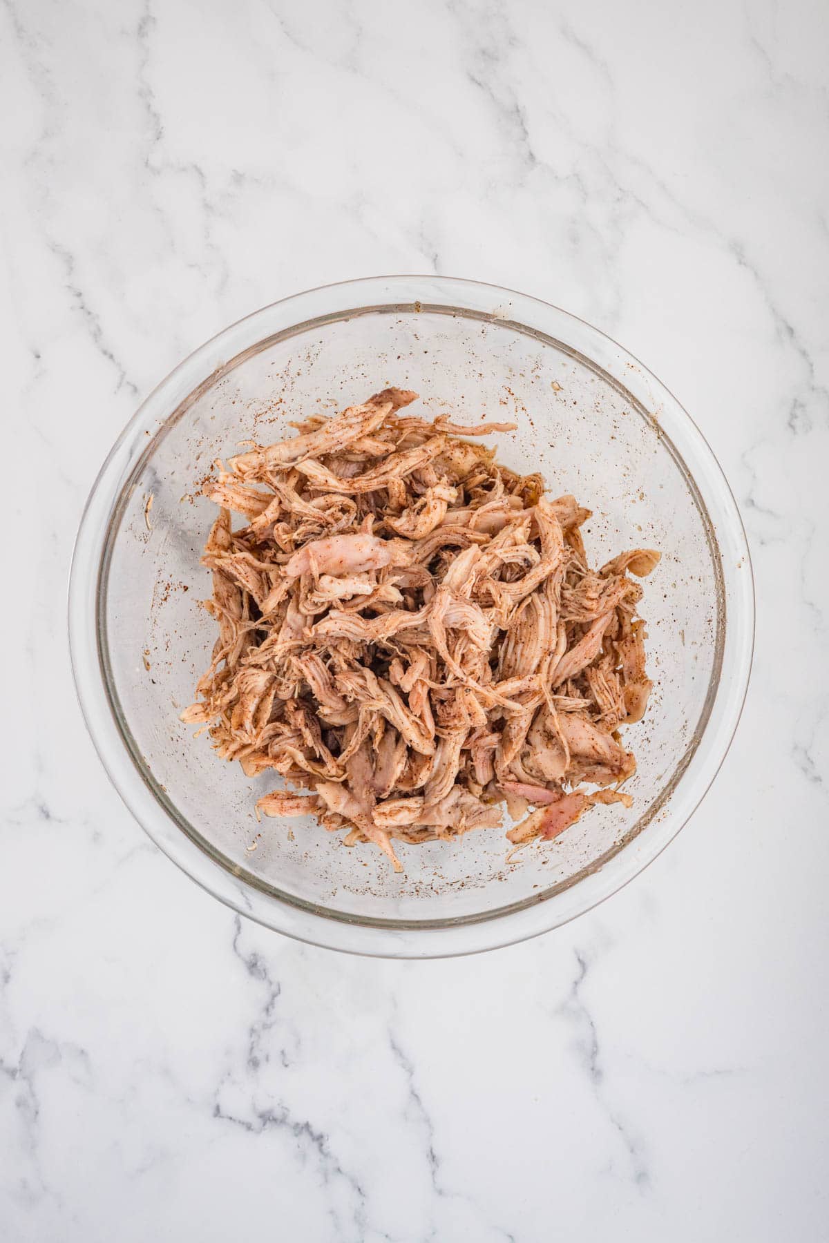 Combining shredded chicken with spices in a mixing bowl.