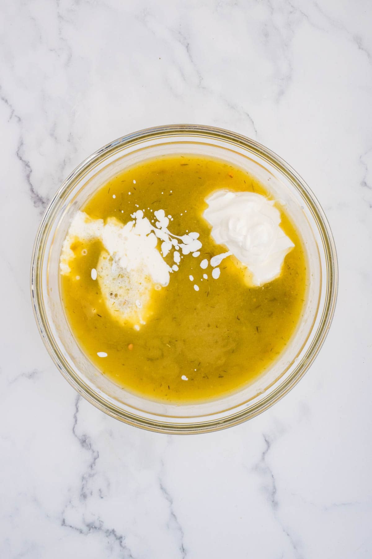 Adding sour cream and heavy cream to green chili enchilada sauce in a glass mixing bowl.