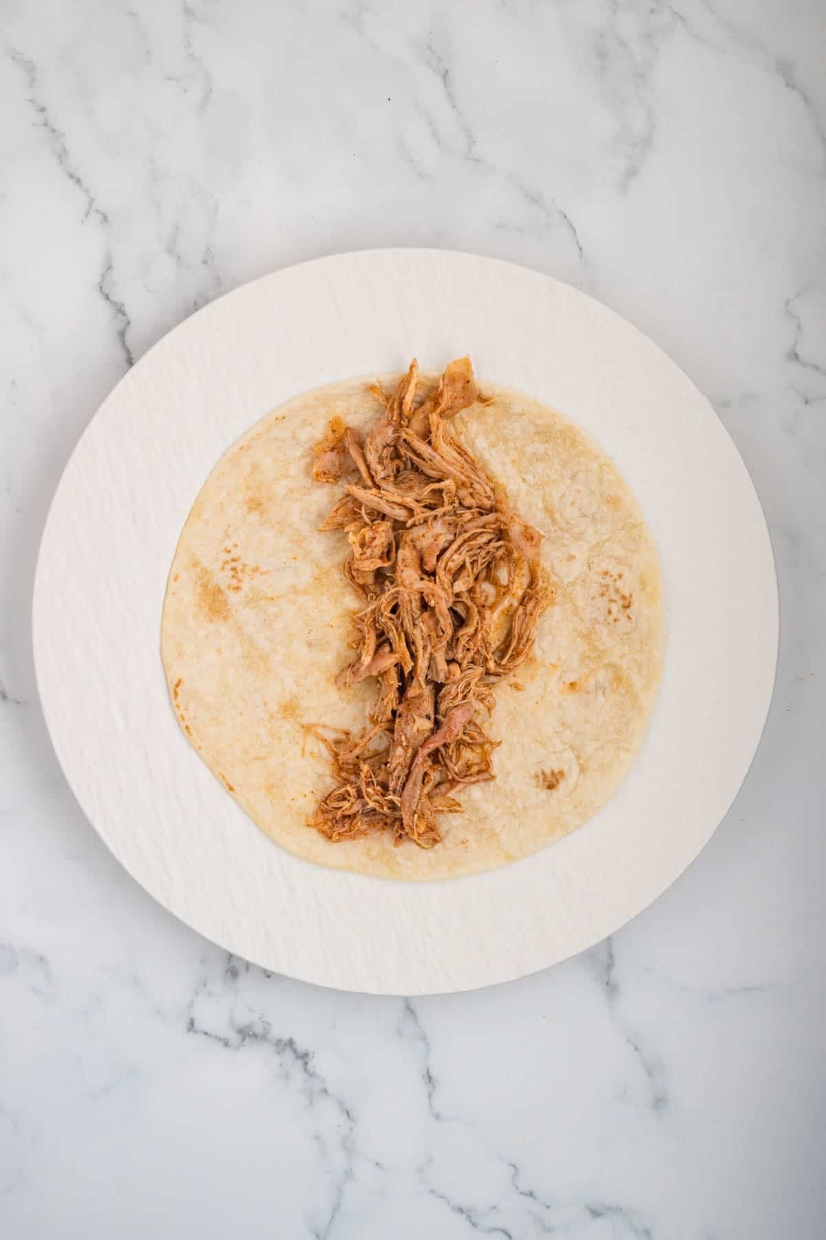A line of shredded chicken on flour tortillas for assembling chicken enchiladas.