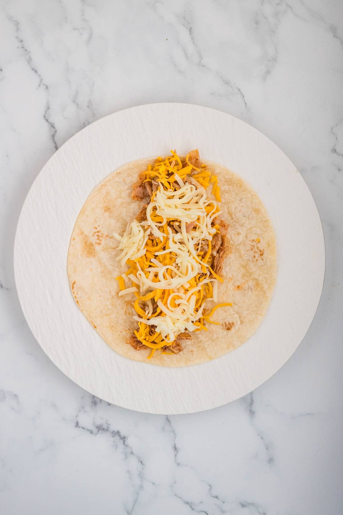 Adding shredded cheese to honey lime chicken enchilada filling.
