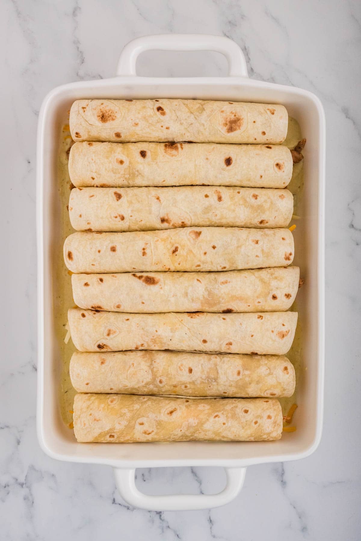 Assembled honey lime chicken enchiladas in a white baking pan.