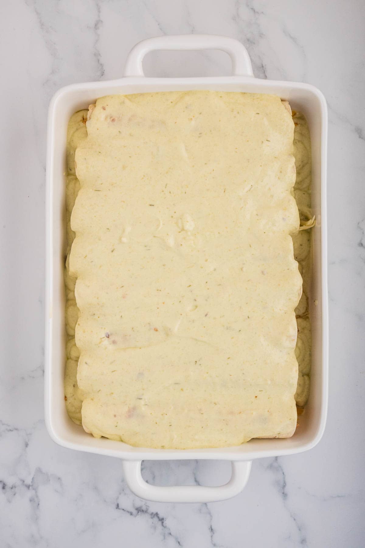 Enchiladas in a baking dish with a creamy sauce poured on top.