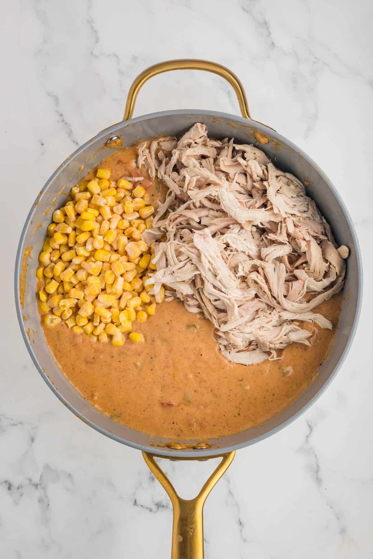 Adding cooked and shredded chicken and corn to a pan of creamy sauce.