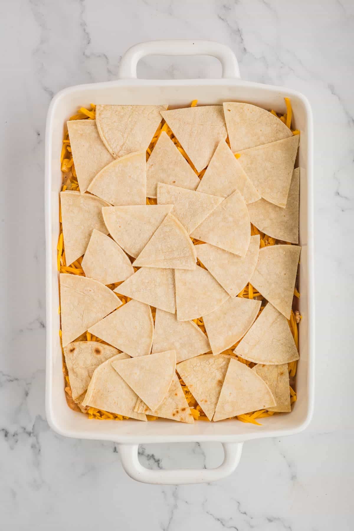 Corn tortillas cut into triangles spread in an even layer in a casserole dish over chicken filling.