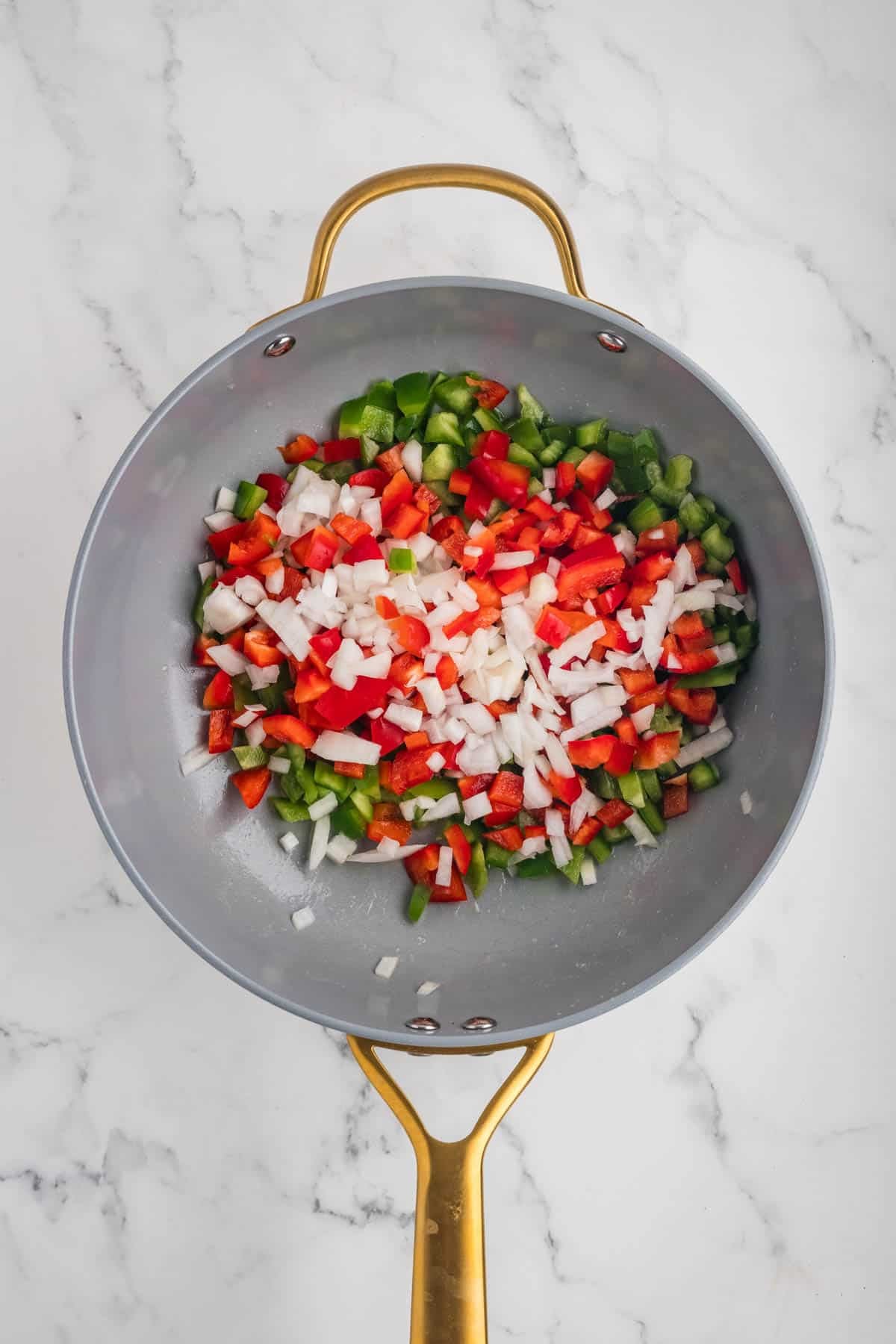 Combining chopped peppers and onions in a skillet.