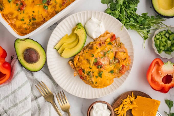 A serving of king ranch chicken on a plate with sliced avocado and sour cream.