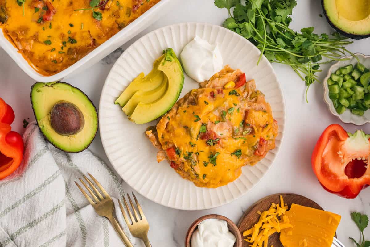A serving of king ranch chicken on a plate with sliced avocado and sour cream.