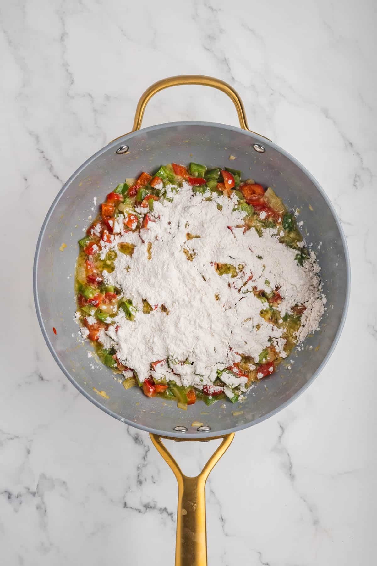 Adding flour to sauteed vegetables in a skillet.