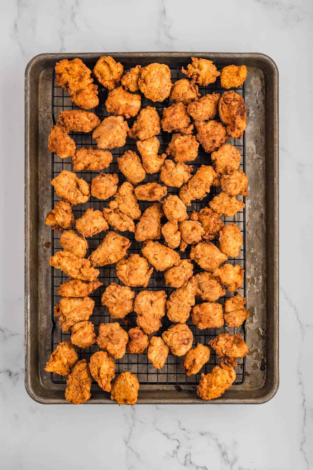 Fried popcorn chicken on a rack over a baking sheet.