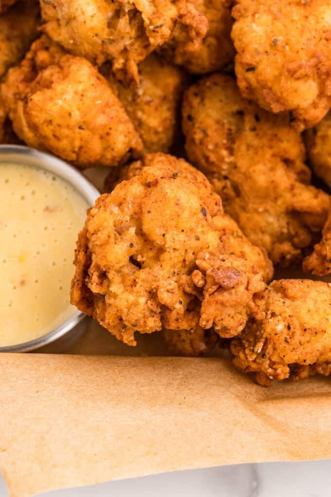 Popcorn chicken pieces next to a small cup of honey mustard dipping sauce.