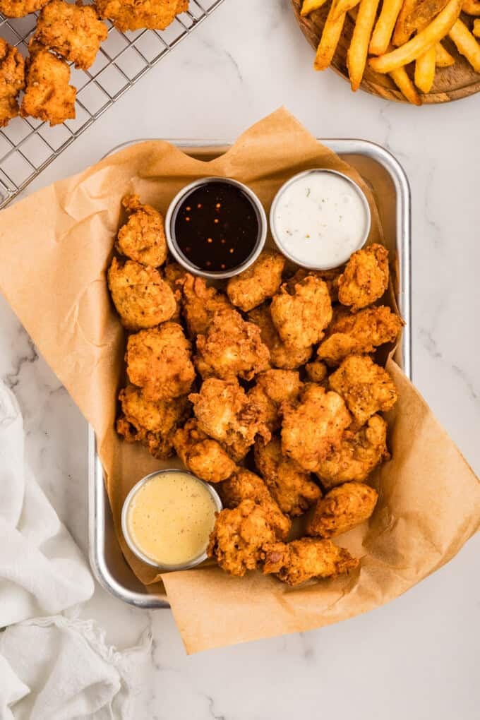 An overhead image of popcorn chicken piled on a small baking sheet with dipping sauces.