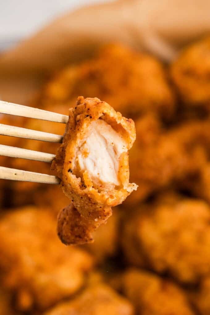 A piece of popcorn chicken with a bite taken out of it on a fork.