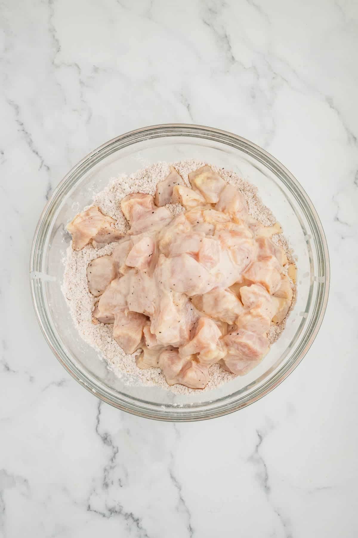 Chicken pieces being dredged in a spiced flour mixture.