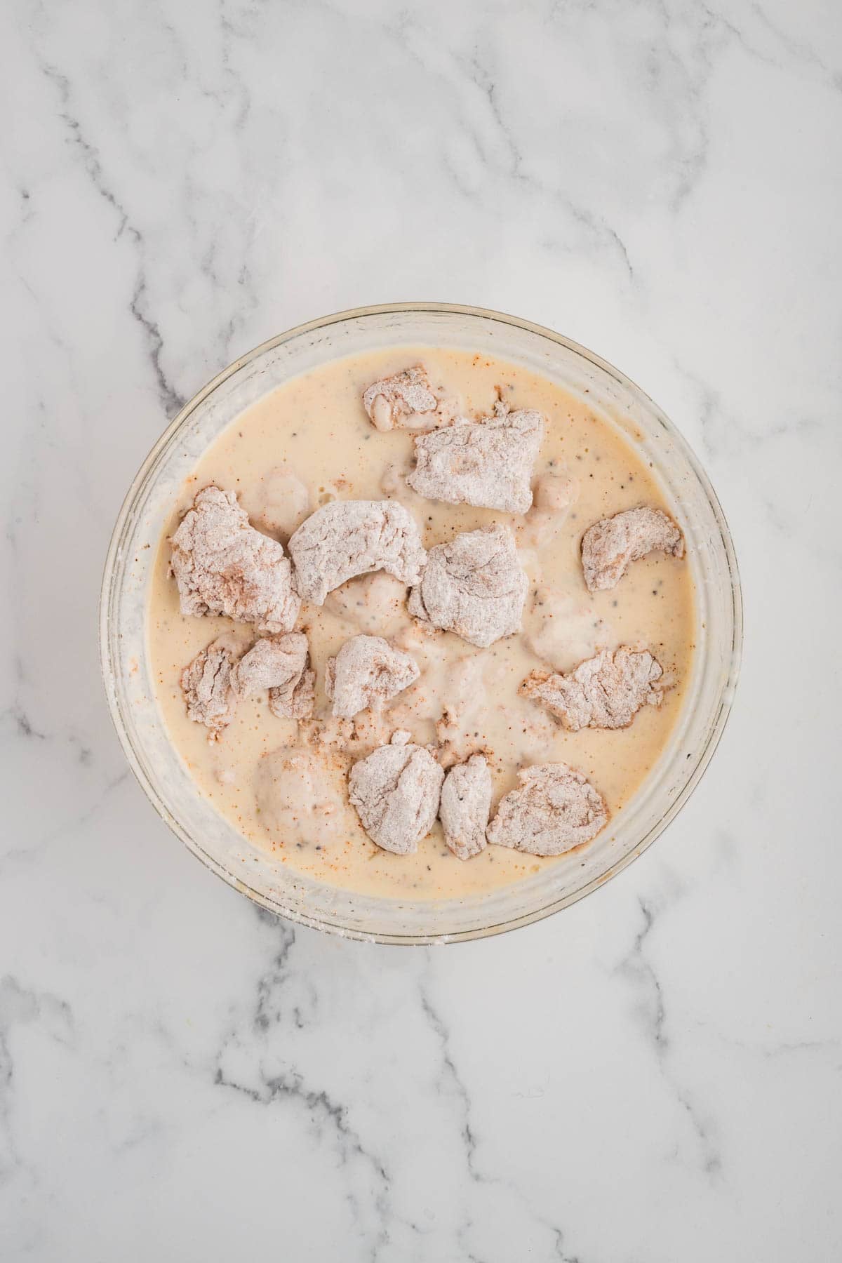 Adding dredged chicken pieces to a buttermilk marinade for a second coating.