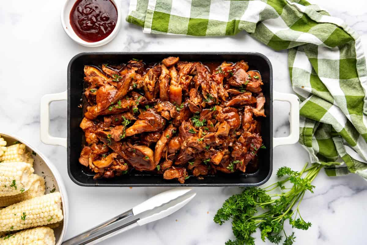 A platter of slow cooker bbq country style ribs next to corn on the cob and a green checked cloth napkin.