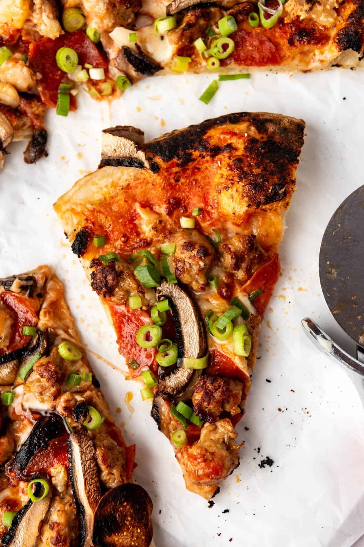 A slice of sourdough pizza topped with mushrooms, sausage, and green onions on a white surface.