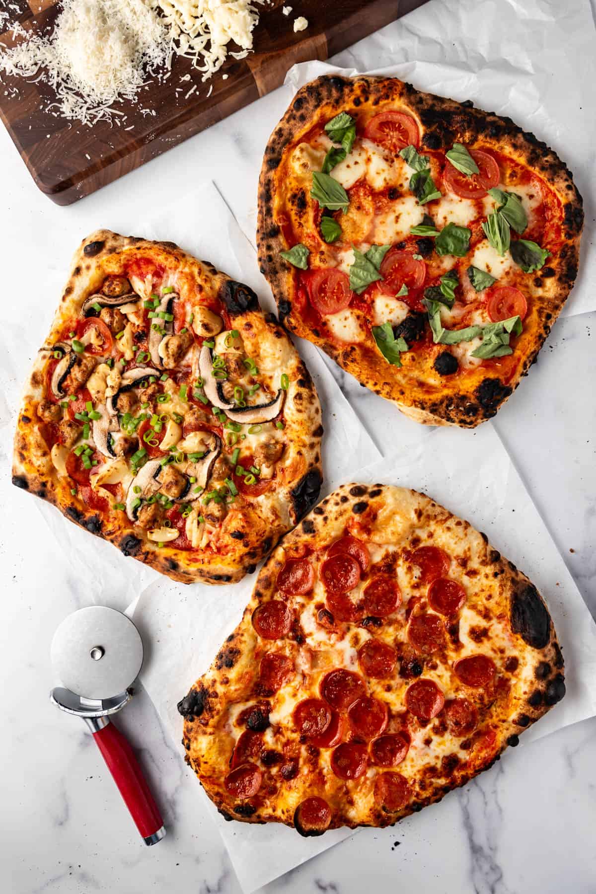 An overhead image of three different sourdough pizzas on a white surface with a pizza cutter nearby.