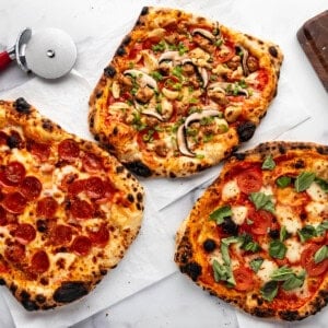An overhead image of three different sourdough pizzas on a white surface with a pizza cutter nearby.